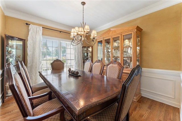 dining room featuring light wood-type flooring, wainscoting, crown molding, and a notable chandelier