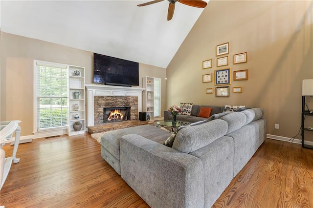 living area with wood finished floors, a fireplace, baseboards, high vaulted ceiling, and a ceiling fan