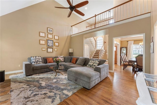 living room with a ceiling fan, a towering ceiling, stairway, baseboards, and light wood finished floors