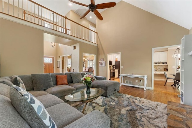 living area with visible vents, light wood finished floors, ceiling fan, and high vaulted ceiling