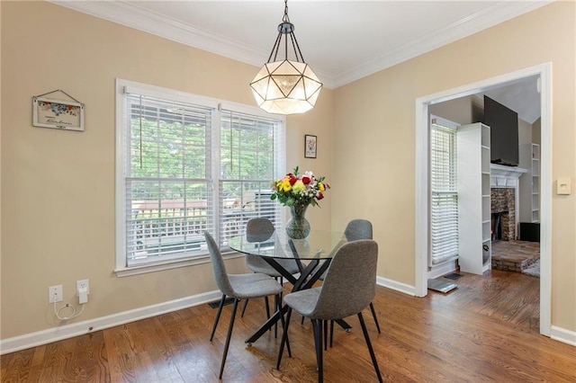 dining room featuring baseboards, ornamental molding, wood finished floors, and a stone fireplace