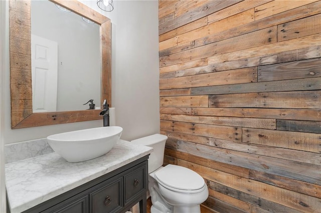 bathroom featuring wooden walls, vanity, and toilet