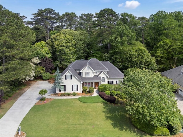 view of front of home with a wooded view, concrete driveway, and a front yard