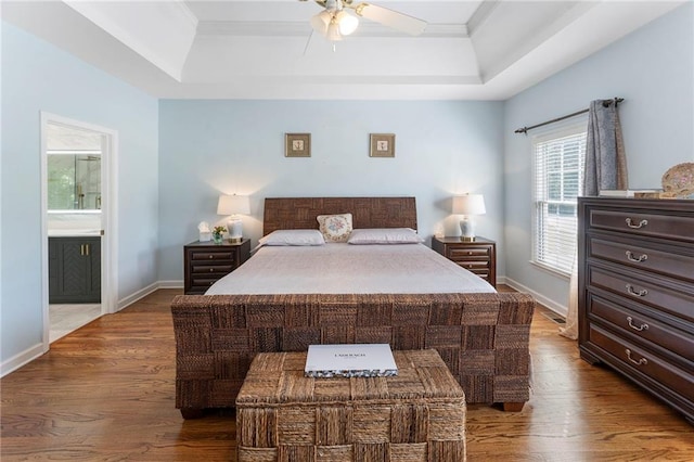 bedroom featuring connected bathroom, baseboards, wood finished floors, a tray ceiling, and ornamental molding