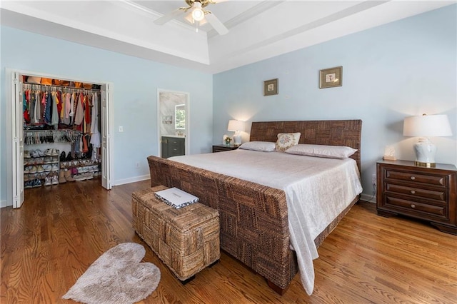 bedroom featuring a ceiling fan, wood finished floors, a raised ceiling, baseboards, and a closet