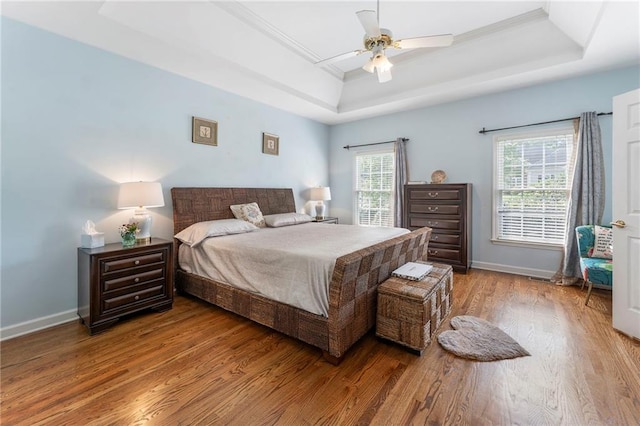 bedroom with crown molding, baseboards, a tray ceiling, and wood finished floors