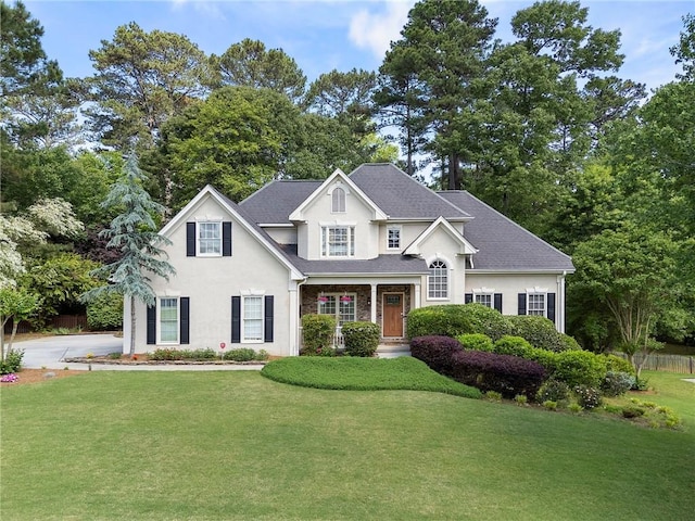 view of front facade featuring a shingled roof, stucco siding, and a front yard