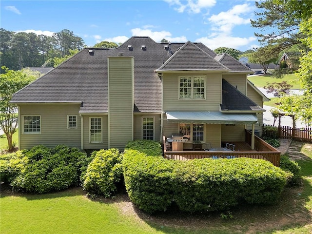 rear view of property featuring fence, roof with shingles, a chimney, and a deck