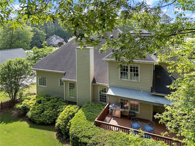rear view of house featuring a chimney, a shingled roof, fence, and a deck