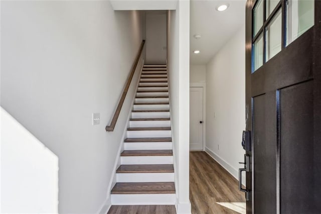 staircase with recessed lighting, wood finished floors, baseboards, and a towering ceiling