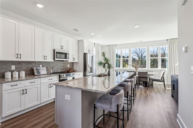 kitchen with a sink, stainless steel appliances, tasteful backsplash, and white cabinets