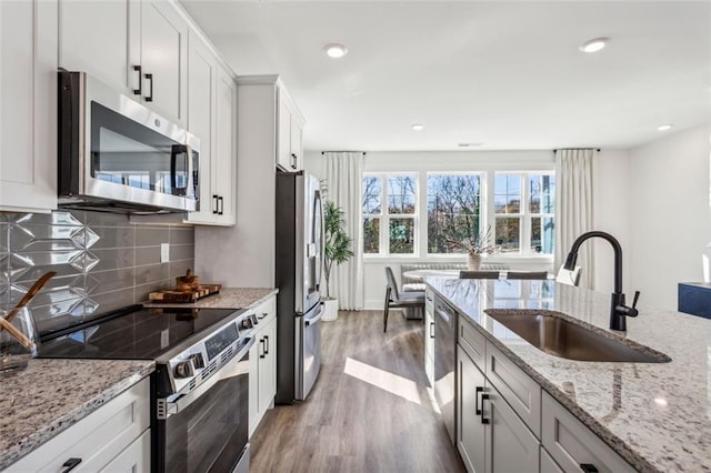 kitchen featuring light wood-style flooring, a sink, tasteful backsplash, appliances with stainless steel finishes, and light stone countertops