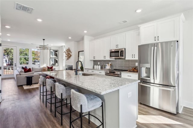 kitchen with visible vents, a center island with sink, a sink, stainless steel appliances, and white cabinets