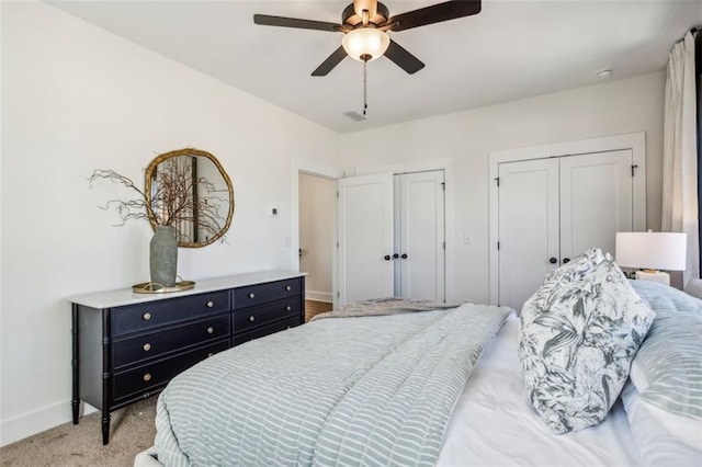 carpeted bedroom with visible vents, baseboards, two closets, and ceiling fan