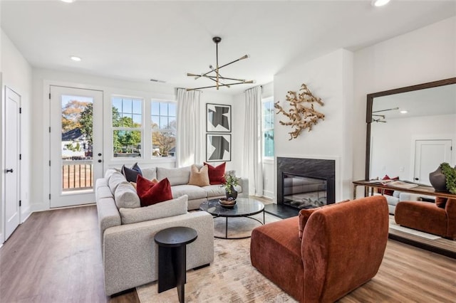 living area featuring wood finished floors, baseboards, recessed lighting, a glass covered fireplace, and a notable chandelier