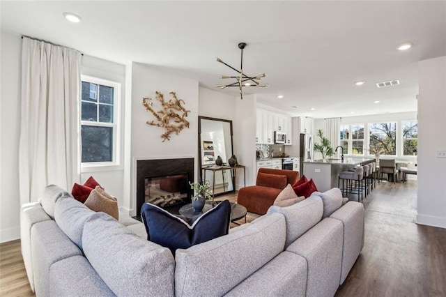 living area featuring wood finished floors, visible vents, baseboards, recessed lighting, and a glass covered fireplace