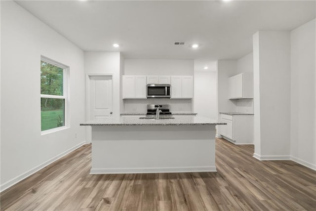 kitchen featuring light wood-type flooring, light stone countertops, white cabinets, and a center island with sink