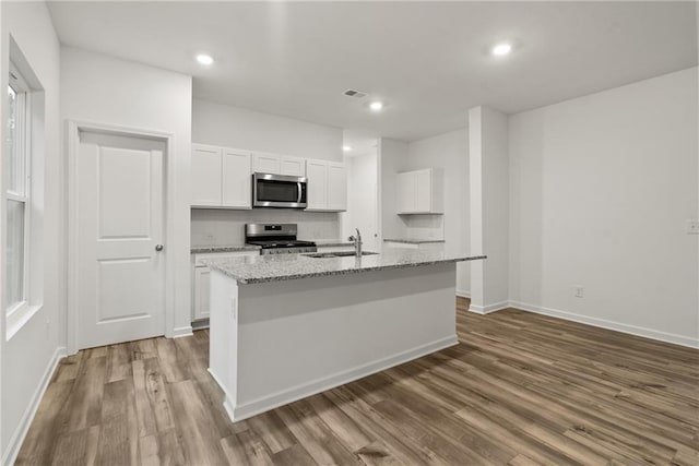 kitchen featuring white cabinetry, light stone counters, stainless steel appliances, and a center island with sink