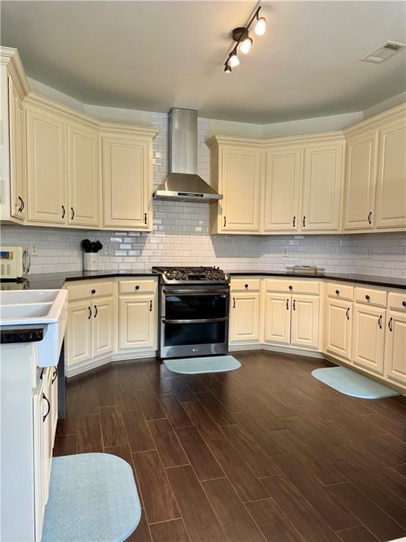 kitchen with visible vents, double oven range, cream cabinetry, and wall chimney range hood