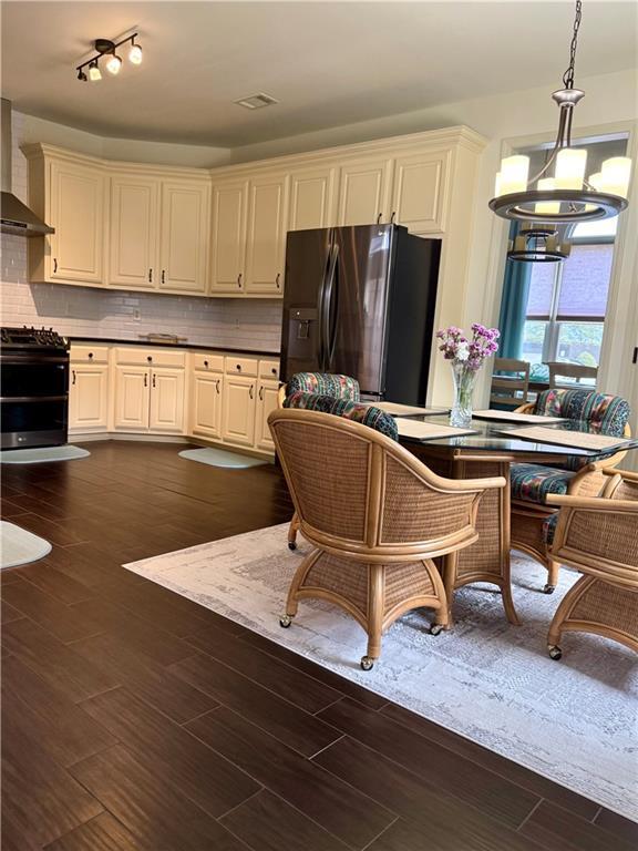 kitchen with backsplash, dark wood finished floors, range with two ovens, black fridge, and cream cabinets