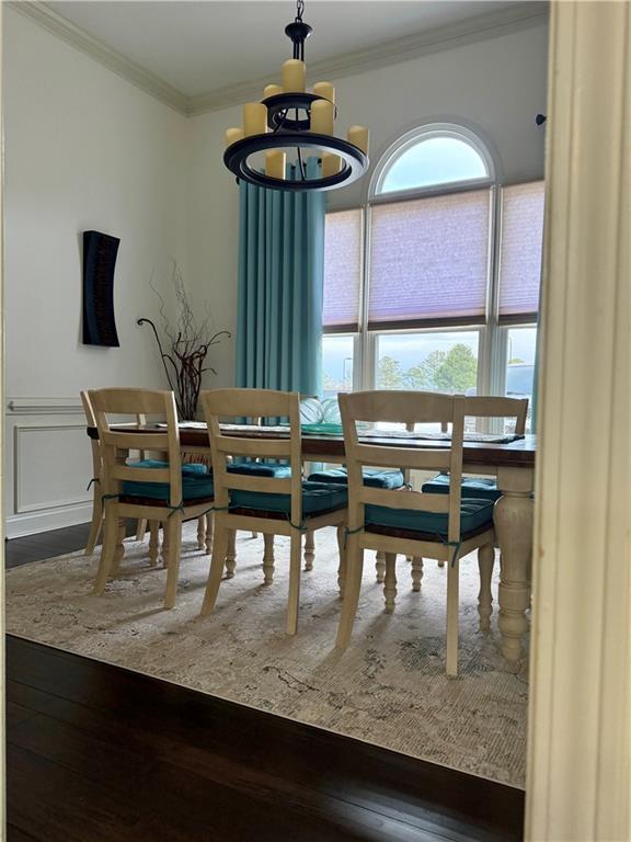 dining space with a wainscoted wall, wood finished floors, ornamental molding, and a decorative wall