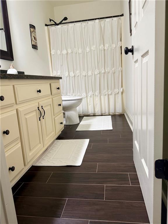 full bathroom with curtained shower, vanity, wood tiled floor, and toilet