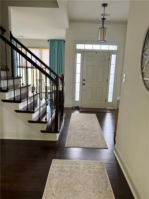 entryway with stairway, visible vents, baseboards, dark wood-style flooring, and ornamental molding