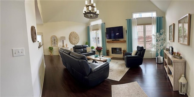 living area featuring a chandelier, a stone fireplace, dark wood finished floors, and vaulted ceiling