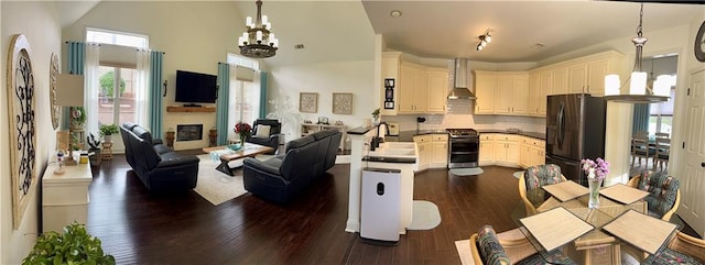 kitchen featuring wall chimney range hood, open floor plan, range with two ovens, black fridge, and an inviting chandelier