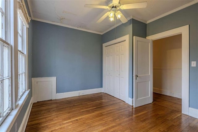 unfurnished bedroom featuring ornamental molding, multiple windows, wood-type flooring, and a closet