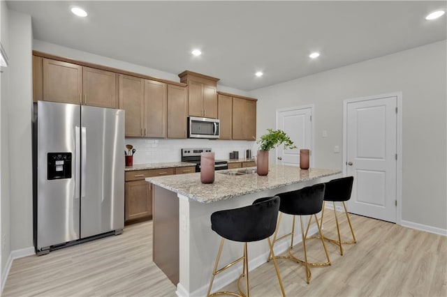 kitchen with stainless steel appliances, recessed lighting, light wood-style flooring, decorative backsplash, and a kitchen breakfast bar