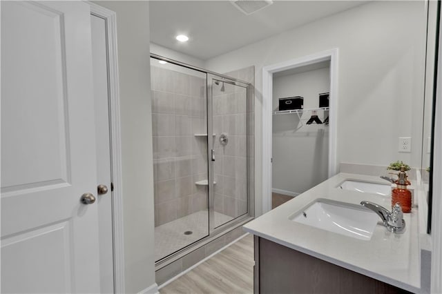 bathroom featuring wood finished floors, a sink, double vanity, a stall shower, and a walk in closet