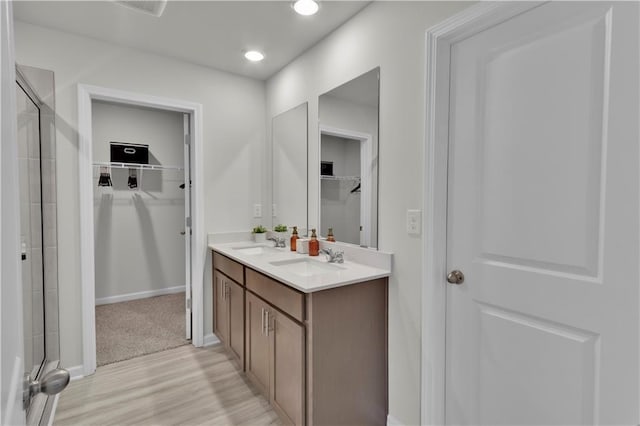 bathroom featuring a spacious closet, double vanity, tiled shower, and a sink