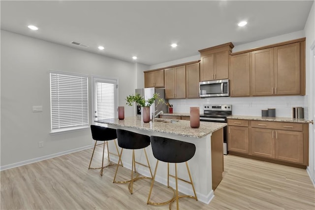 kitchen with stainless steel appliances, light wood-style flooring, decorative backsplash, an island with sink, and a kitchen bar