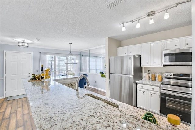 kitchen with sink, white cabinets, hanging light fixtures, and stainless steel appliances