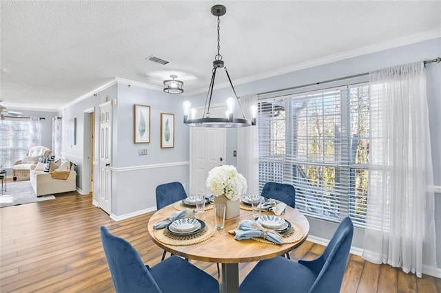 dining room featuring a textured ceiling, hardwood / wood-style flooring, ceiling fan with notable chandelier, and ornamental molding