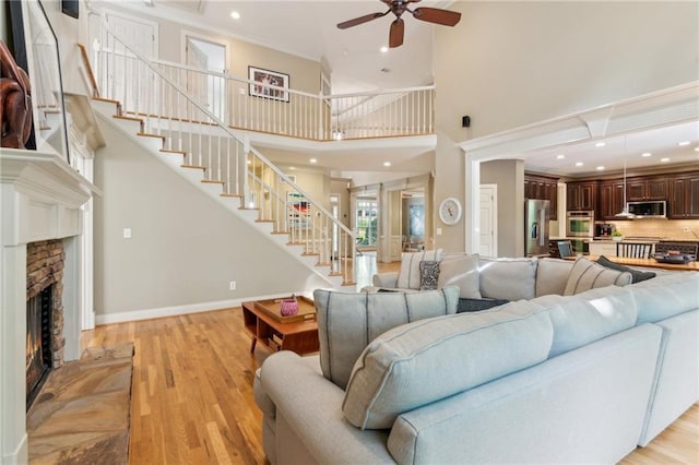 6795 Preston Glen Dr, Alpharetta, GA 30005 - living room featuring stairway, a high ceiling, light wood-type flooring, ceiling fan, and a warm lit fireplace