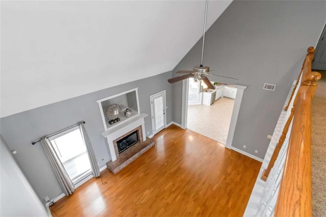 1027 Eagles Brooke Dr, Locust Grove, GA 30248 - unfurnished living room with visible vents, a ceiling fan, light wood-style flooring, a brick fireplace, and high vaulted ceiling