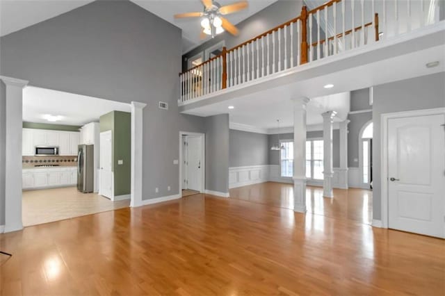 1027 Eagles Brooke Dr, Locust Grove, GA 30248 - unfurnished living room featuring a ceiling fan, a towering ceiling, light wood finished floors, visible vents, and decorative columns