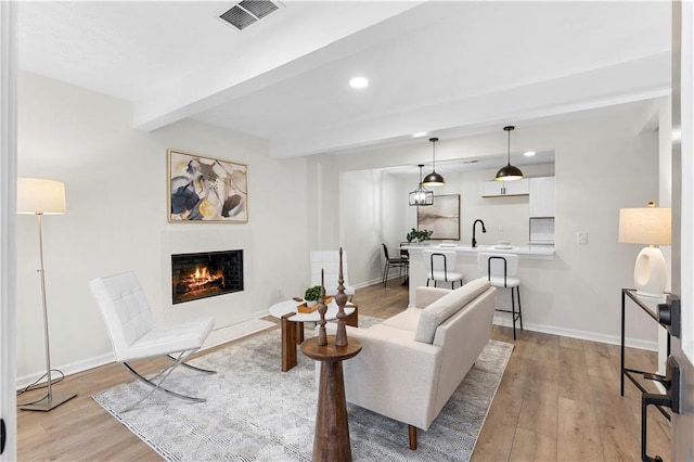 living room with beam ceiling, light wood-type flooring, and sink