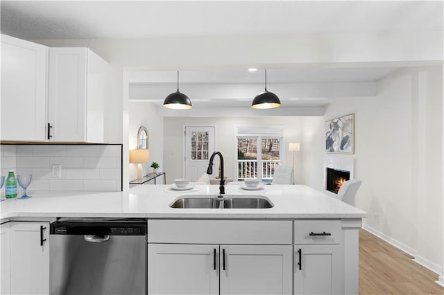 kitchen with stainless steel dishwasher, pendant lighting, backsplash, white cabinetry, and sink