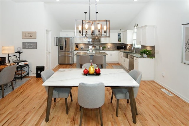 dining area featuring sink, high vaulted ceiling, a chandelier, and light wood-type flooring