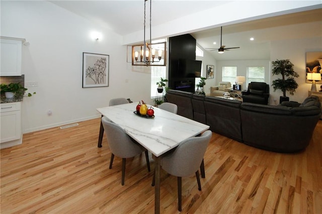 dining space featuring ceiling fan with notable chandelier, light hardwood / wood-style flooring, and lofted ceiling