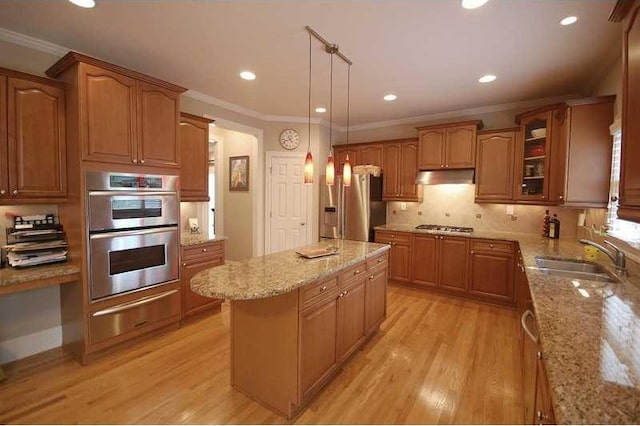 kitchen with a sink, under cabinet range hood, stainless steel appliances, a kitchen island, and light stone counters