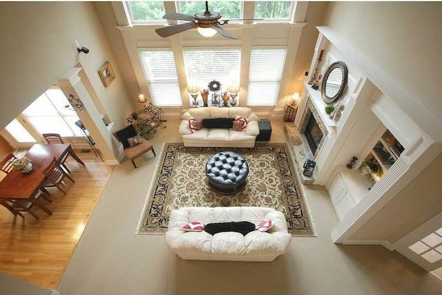 living area with a fireplace, a towering ceiling, wood finished floors, and ceiling fan