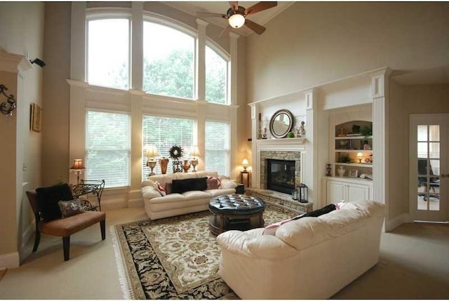 living room featuring built in features, a fireplace, a high ceiling, ceiling fan, and carpet