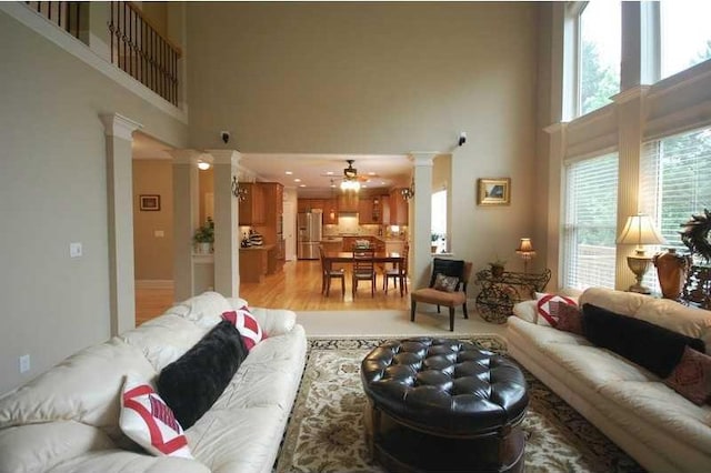 living area with decorative columns, light wood finished floors, a high ceiling, and a ceiling fan