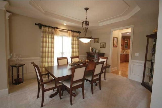 dining room with a decorative wall, a tray ceiling, crown molding, and a wainscoted wall
