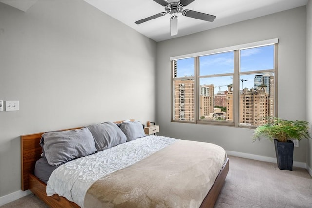 bedroom with a view of city, ceiling fan, baseboards, and light colored carpet