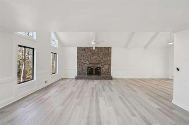 unfurnished living room featuring lofted ceiling with beams, light wood-type flooring, a stone fireplace, and a ceiling fan